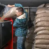 Mężczyzna wsypuje do kotła **co to jest pellet do ogrzewania**, obok stosy worków z tym ekologicznym paliwem.