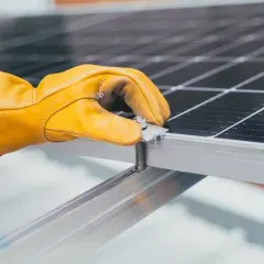 Ręka w żółtej rękawicy dokręca śrubę mocującą panel słoneczny. To ważny krok, by wiedzieć, jak dobrać falownik do instalacji.