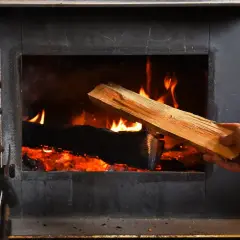 Ręka wkłada do paleniska świeże drewno. Jaka wilgotność drewna do kominka jest najlepsza? Suche drewno pali się efektywniej.