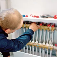 Instalator reguluje rozdzielacz ogrzewania podłogowego. To kluczowy etap, by przerobić grzejnik na ogrzewanie podłogowe.