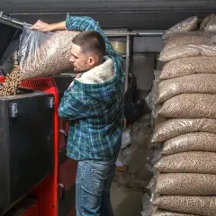Mężczyzna wsypuje do kotła **co to jest pellet do ogrzewania**, obok stosy worków z tym ekologicznym paliwem.