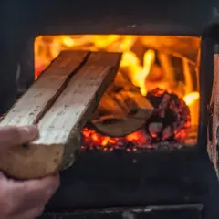 Ręka wkłada drewno do paleniska. Czy można palić drewnem w piecu na ekogroszek? Ogień płonie jasno.