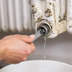 Ręka z kluczem odkręca zawór grzejnika, z którego kapie woda. Dowiedz się, jak wymienić zawór w grzejniku bez spuszczania wody.