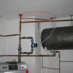 Instalacja hydrauliczna z bojlerem i pompą obiegową. Pokazano fragment instalacji, jak podłączyć zawór bezpieczeństwa do bojlera, z widocznymi rurami miedzianymi i złączkami.