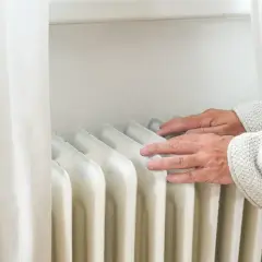 Dłonie sprawdzają temperaturę grzejnika, zastanawiając się, dlaczego grzejnik grzeje tylko do połowy.