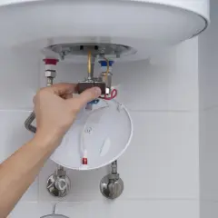 Ręka majstruje przy bojlerze, przygotowując się do wymiany grzałki. Czy trzeba spuścić wodę? To kluczowe pytanie przy tej naprawie.