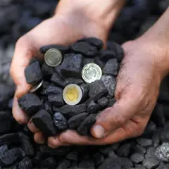 Dłonie trzymają węgiel i monety. Zastanawiasz się, ile kosztuje tona ekogroszku?