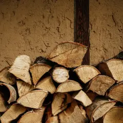 Stos drewna opałowego przy glinianej ścianie. Zastanawiasz się, ile kosztuje kubik drzewa?