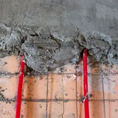 Czerwone rury ogrzewania podłogowego pod świeżą wylewką betonową. Kluczowe jest odpowiednie dobranie grubości wylewki, by zapewnić efektywne rozprowadzanie ciepła.