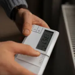 Ręka reguluje termostat, szukając optymalnej wartości, jaką temperaturę ustawić na piecu gazowym kondensacyjnym przy podłogówce.