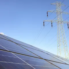 Panele fotowoltaiczne i linia energetyczna pod błękitnym niebem. Zastanawiasz się, jak zresetować fotowoltaikę?