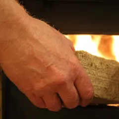 Dłoń wkłada brykiet z liści do rozpalonego pieca.