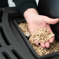 Dłoń wsypuje pellet do zasobnika. Czy palenie pelletem będzie zakazane? Ekogroszek i pellet to popularne paliwa.