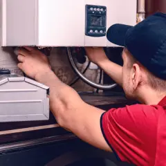 Instalator pracuje przy kotle gazowym, podłączając przewody. W tle widać metalową skrzynkę, która może być pomocna, gdy zastanawiamy się, jak zalać grzejnik elektryczny.