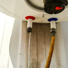 Woda kapie z bojlera od spodu. Widać dwa węże podłączone do urządzenia, jeden z nich jest mokry.