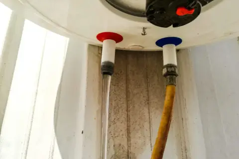 Woda kapie z bojlera od spodu. Widać dwa węże podłączone do urządzenia, jeden z nich jest mokry.