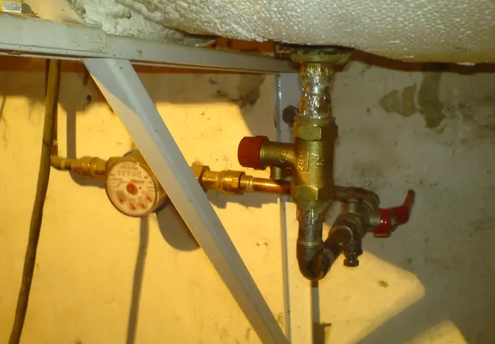 Instrukcja jak zamontować zawór bezpieczeństwa przy bojlerze. Widoczny wodomierz i instalacja wodna.