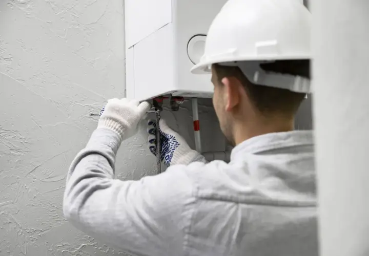 Fachowiec w białym kasku i rękawicach montuje bojler elektryczny, podłączając rury.