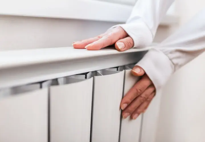 Dłonie na grzejniku, sprawdzające temperaturę. Czas pomyśleć, kiedy wyłączyć ogrzewanie podłogowe.