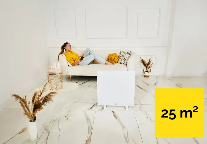 Kobieta relaksuje się na kanapie, podczas gdy panel grzewczy na podczerwień ogrzewa pomieszczenie 25 m².