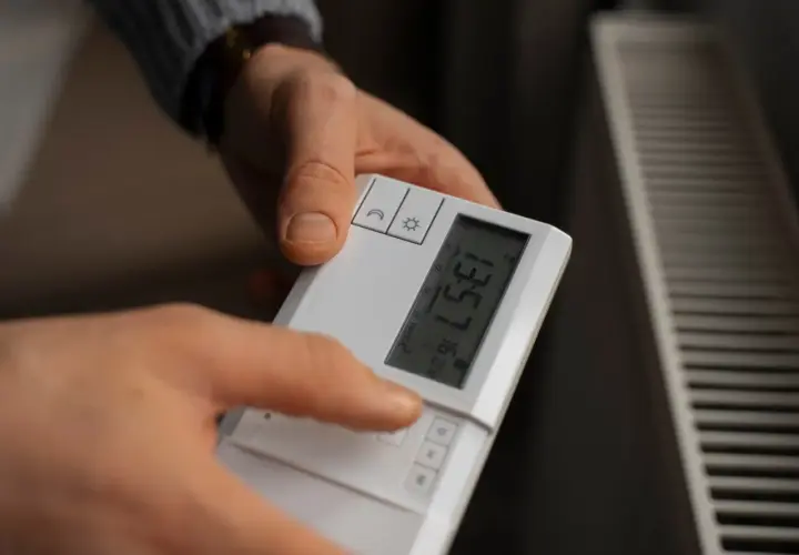 Ręka reguluje termostat, szukając optymalnej wartości, jaką temperaturę ustawić na piecu gazowym kondensacyjnym przy podłogówce.