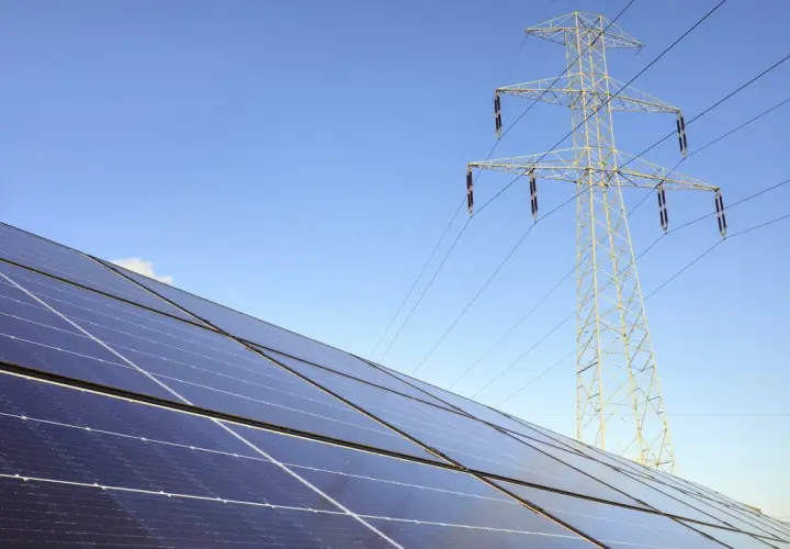 Panele fotowoltaiczne i linia energetyczna pod błękitnym niebem. Zastanawiasz się, jak zresetować fotowoltaikę?