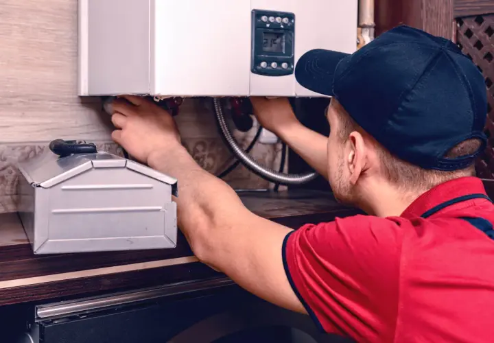 Instalator pracuje przy kotle gazowym, podłączając przewody. W tle widać metalową skrzynkę, która może być pomocna, gdy zastanawiamy się, jak zalać grzejnik elektryczny.