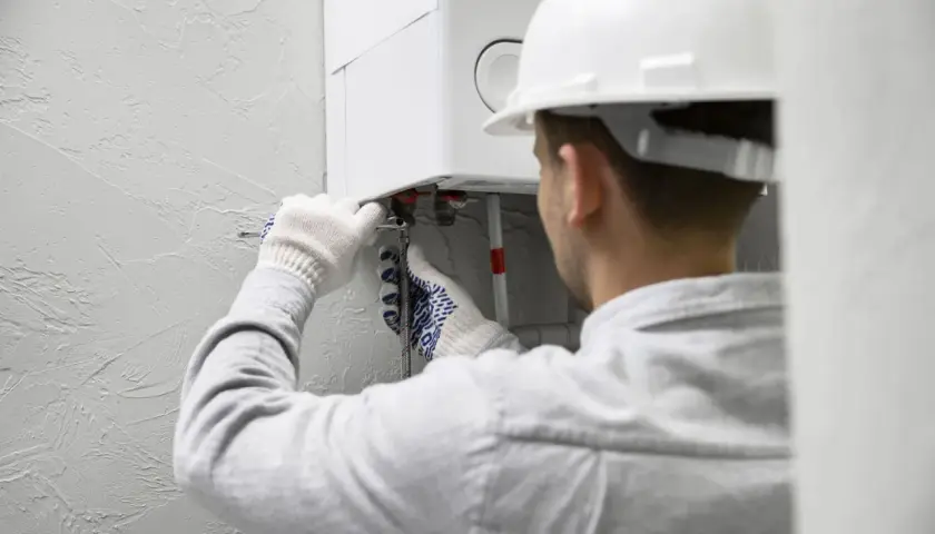 Fachowiec w białym kasku i rękawicach montuje bojler elektryczny, podłączając rury.