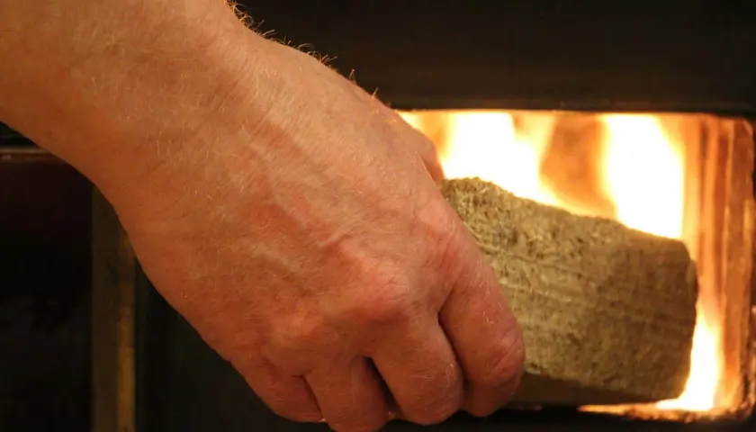 Dłoń wkłada brykiet z liści do rozpalonego pieca.
