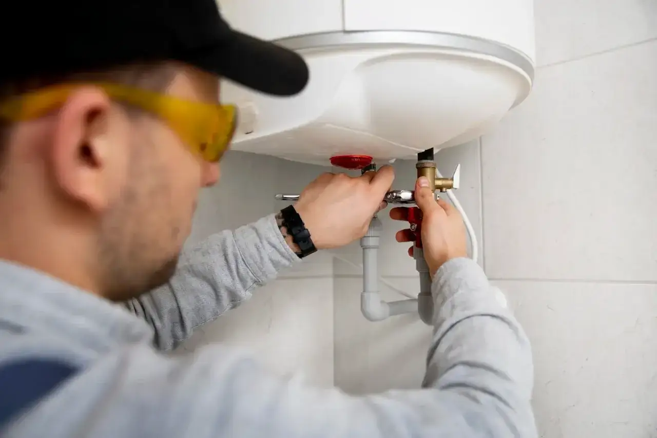 Fachowiec w okularach ochronnych dokonuje montażu bojlera elektrycznego, podłączając rury.